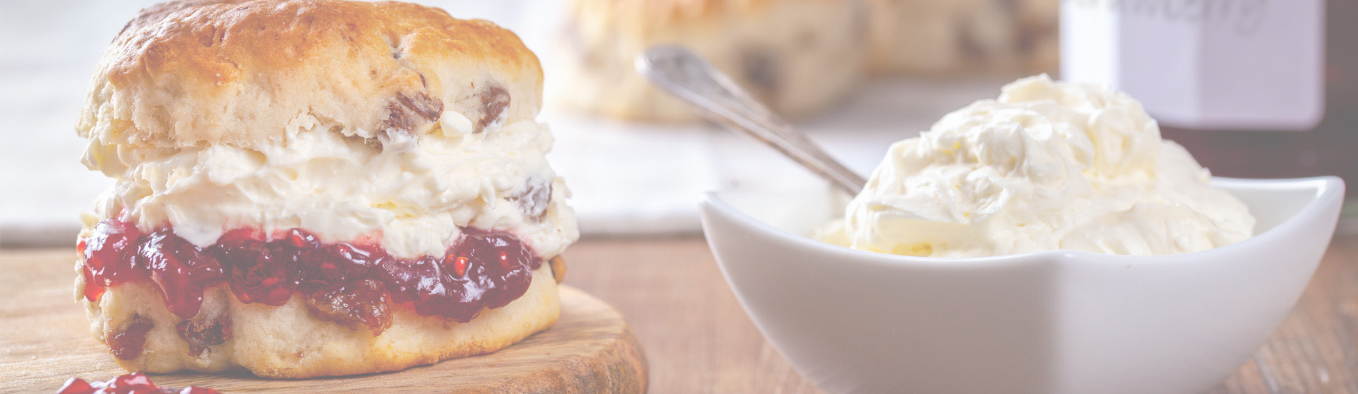 Tafel met links een scone met jam en clotted cream erop en rechts een schaaltje met clotted cream en lepel erin